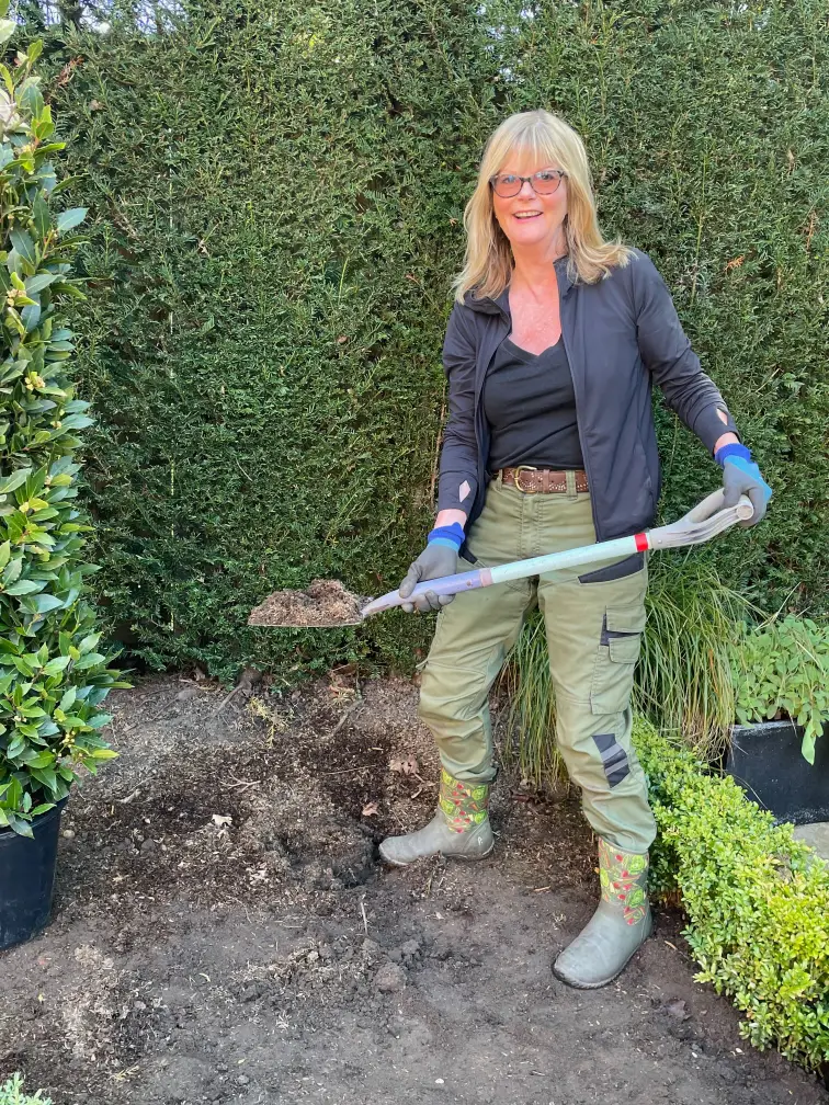 Michaela Day Garden Designer with a shovel full of soil in plant bed.